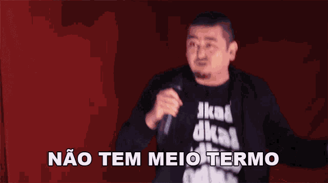 a man holding a microphone in front of a red curtain with the words não tem meio termo