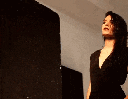 a woman in a black dress is standing in a room with her eyes closed .