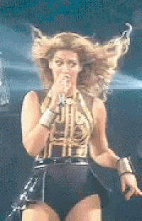 a woman is singing into a microphone on a stage while her hair is blowing in the wind .