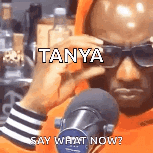 a man wearing sunglasses and a hoodie is talking into a microphone and saying tanya say what now ?