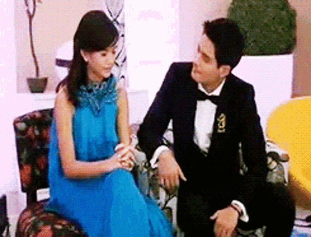 a man in a tuxedo and a woman in a blue dress are sitting on a couch