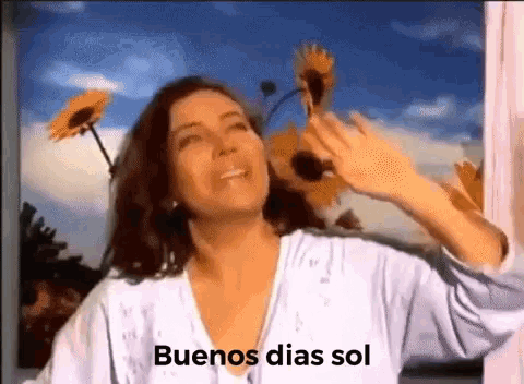 a woman is standing in front of a window with sunflowers in the background and the words buenos dias sol on the bottom .