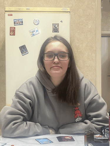 a girl wearing glasses sits at a table in front of a refrigerator