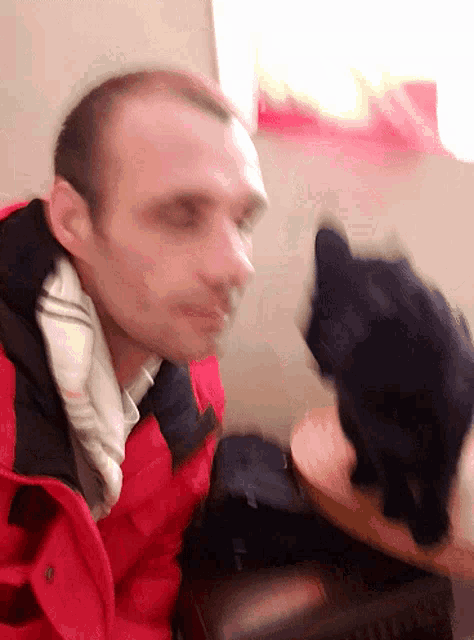 a man in a red jacket is sitting next to a black cat