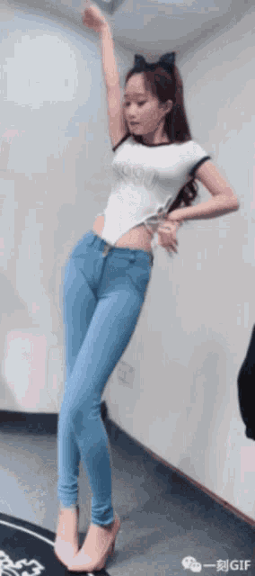 a woman in a white top and blue jeans is dancing with her arms in the air