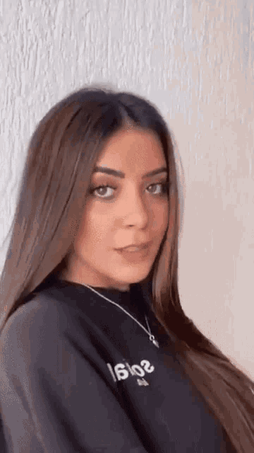 a woman with long brown hair is wearing a black sweater and a necklace .