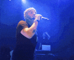 a man with a tattoo on his arm sings into a microphone on stage