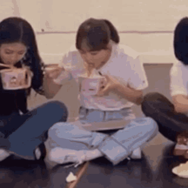 a group of young women are sitting on the floor eating noodles with chopsticks .