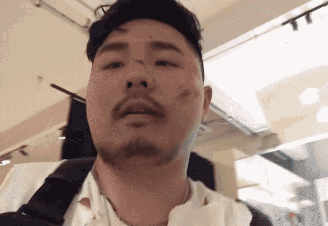 a man with a beard is wearing a white shirt and a black necklace