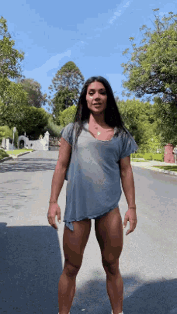 a woman in a grey shirt and shorts is standing on the side of the road
