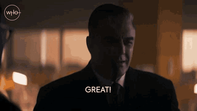 a man in a suit and tie says great in a dark room