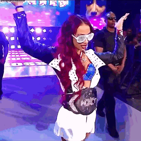 a woman with red hair and sunglasses is standing on a stage with her hands in the air .