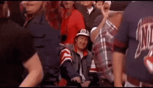 a man in a hat is sitting in the stands watching a game .
