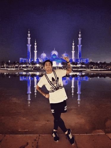 a man in a white adidas shirt stands in front of a mosque