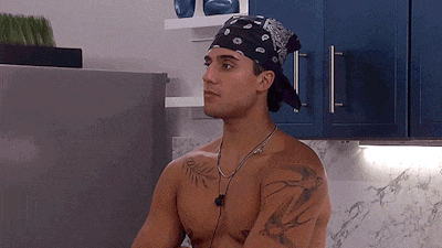 a shirtless man wearing a bandana and ear buds in a kitchen