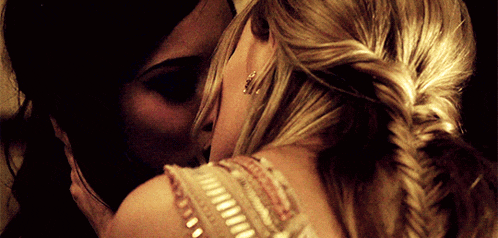 a close up of two women kissing with one wearing earrings
