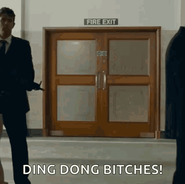 a man in a suit and tie stands in front of a fire exit