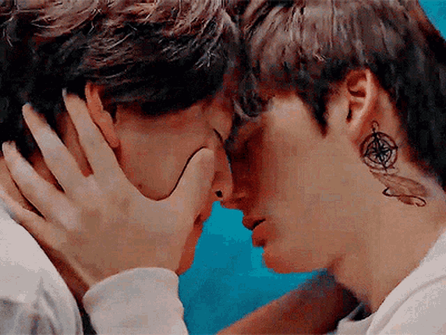 a man with a compass tattoo on his neck is kissing another man .