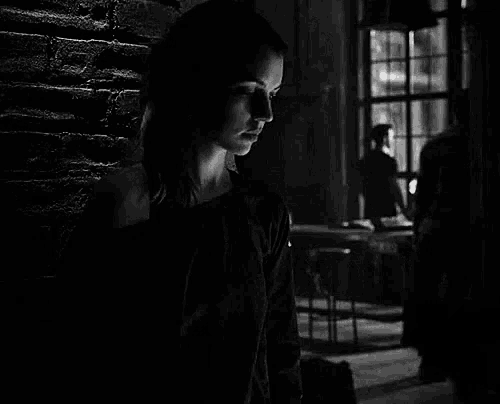 a woman is leaning against a brick wall in a dark room