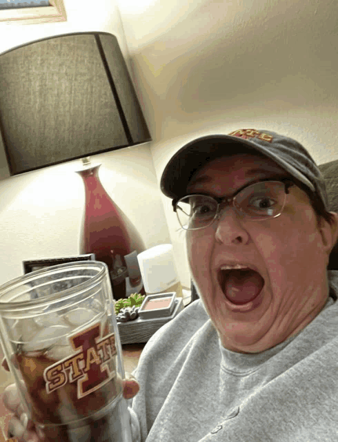 a woman wearing a hat and glasses is holding a glass that says state