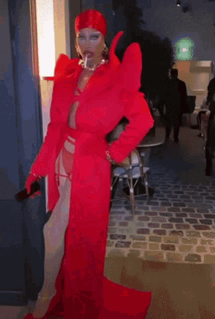 a drag queen is wearing a red outfit and holding a sword .