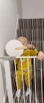 a baby is sitting on a set of stairs behind a fence holding a toy .