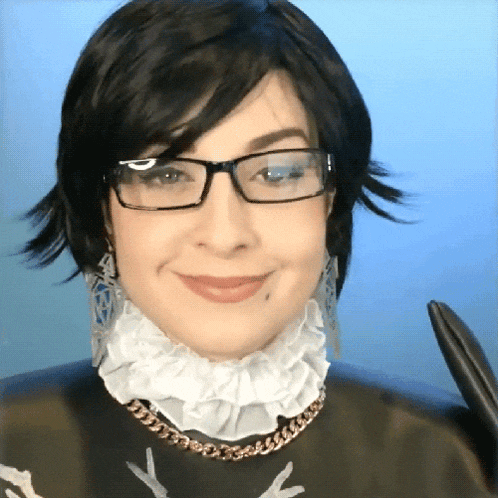 a woman wearing glasses and a ruffled collar smiles for the camera