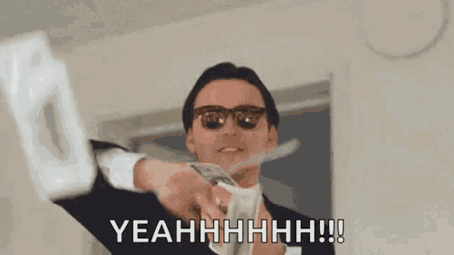 a man in a suit and sunglasses is holding a bunch of money in his hand .