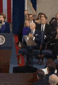 a man in a suit sits in front of a podium with the president 's seal on it