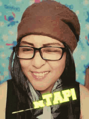 a woman wearing glasses and a beanie is smiling and making a funny face .