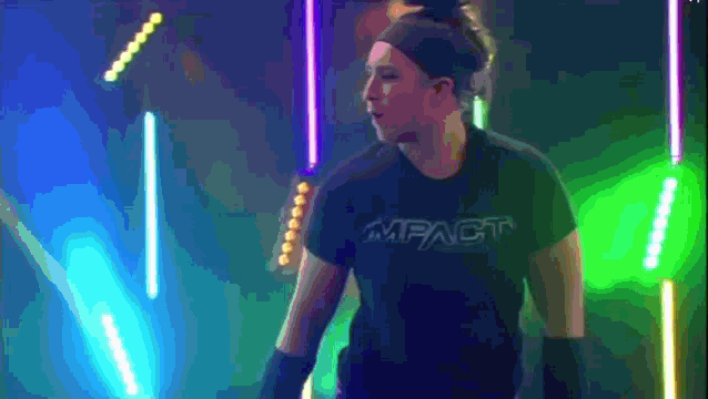 a woman wearing a black impact shirt stands in a dark room