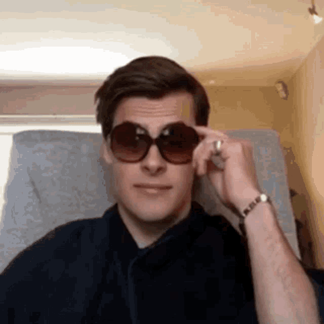 a man wearing sunglasses is sitting in a chair and adjusting his sunglasses .
