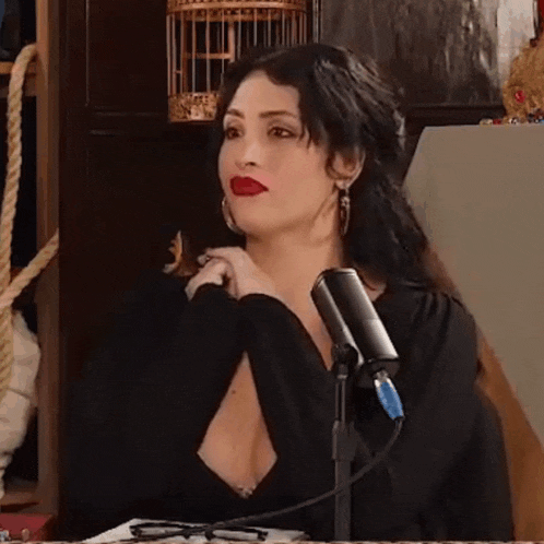 a woman in a black dress is sitting in front of a microphone and looking at the camera .