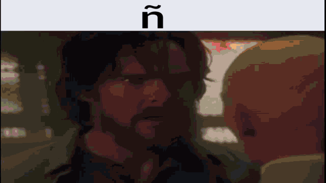 a man with a beard is looking at another man with the letters ñ on the bottom