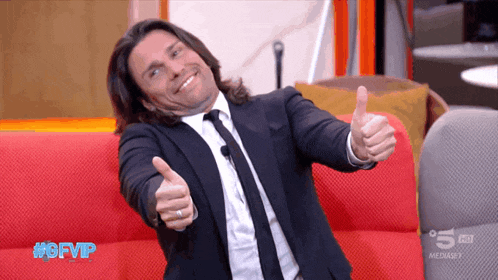 a man in a suit and tie gives a thumbs up sign