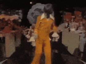 a man in a yellow suit is dancing in front of a crowd .