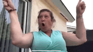a woman in a blue tank top is standing in front of a window with her arms in the air .