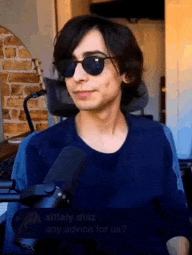 a man wearing sunglasses and a blue shirt is holding a microphone .