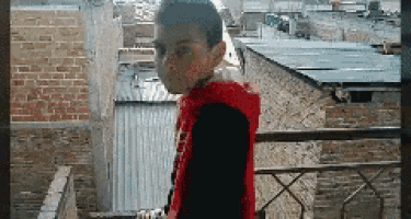 a boy in a red hoodie stands on a balcony