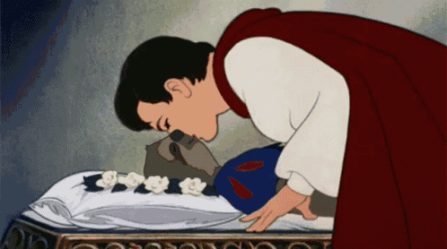 a man in a red cape kisses the face of a sleeping snow white