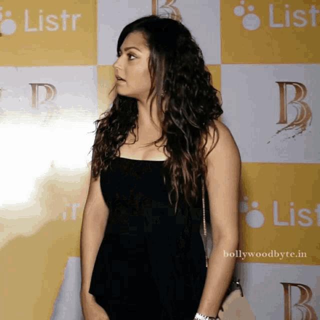 a woman in a black top stands in front of a wall with the letter b on it