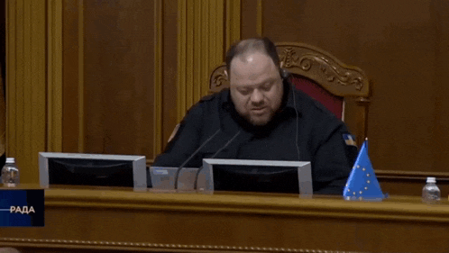 a man sits at a desk with a sign that says " rada "