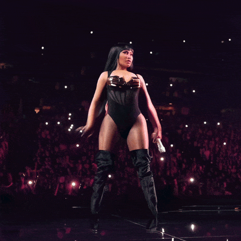 a woman in a black bodysuit is holding a microphone in front of a large crowd