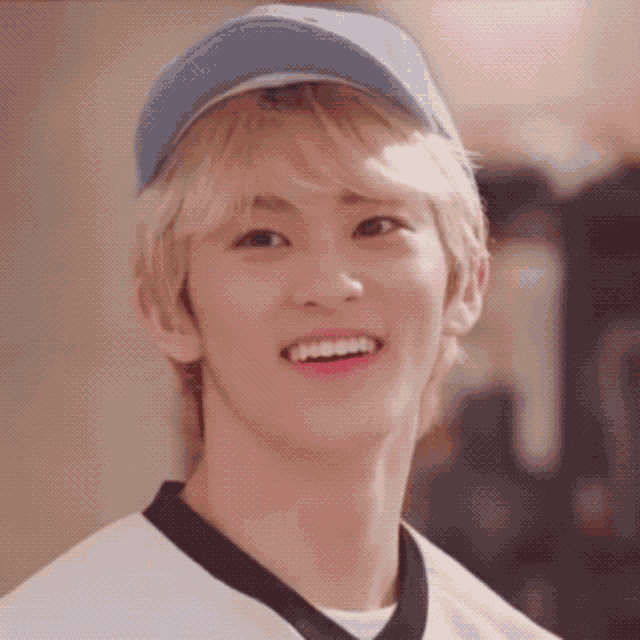 a young man wearing a blue hat and a white shirt smiles for the camera