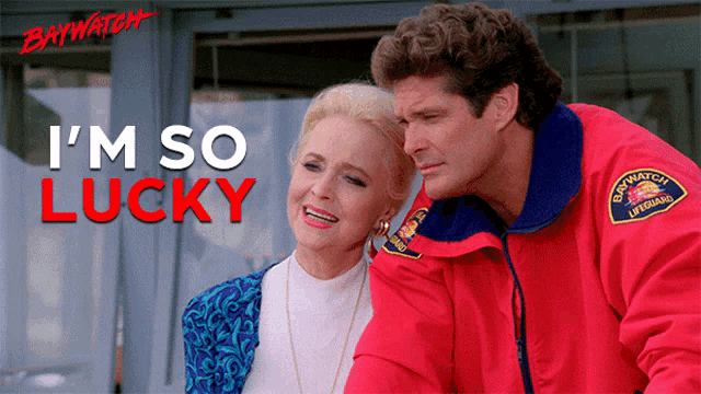 a man in a red baywatch jacket stands next to an older woman