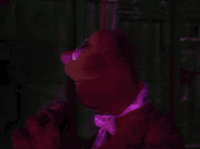 a stuffed animal with a purple face is standing in a dark room with a purple light behind it