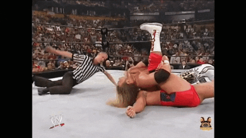 two wrestlers are wrestling in a wrestling ring with a referee .