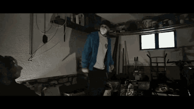 a man wearing a mask and a blue jacket is standing in a garage
