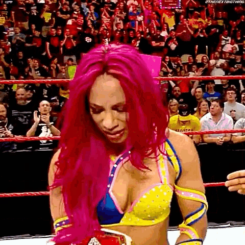a woman with pink hair is in a wrestling ring with a crowd watching .