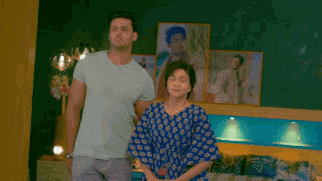 a man and a woman are dancing in a bedroom with pictures on the wall behind them